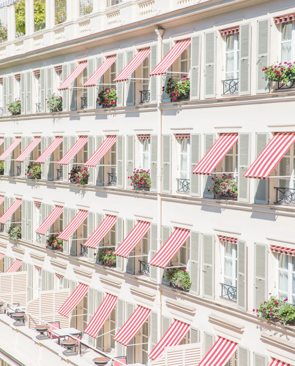 French building with red-and-white awnings over flower-decorated balconies