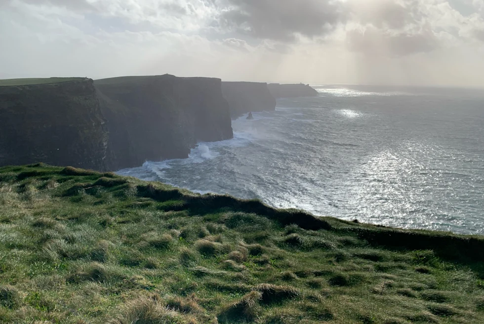 dramtic grassy clif into the sea with sun beaming through thick clouds