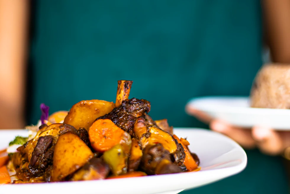 Person wearing teal apron holding plate of Jamaican jerk chicken