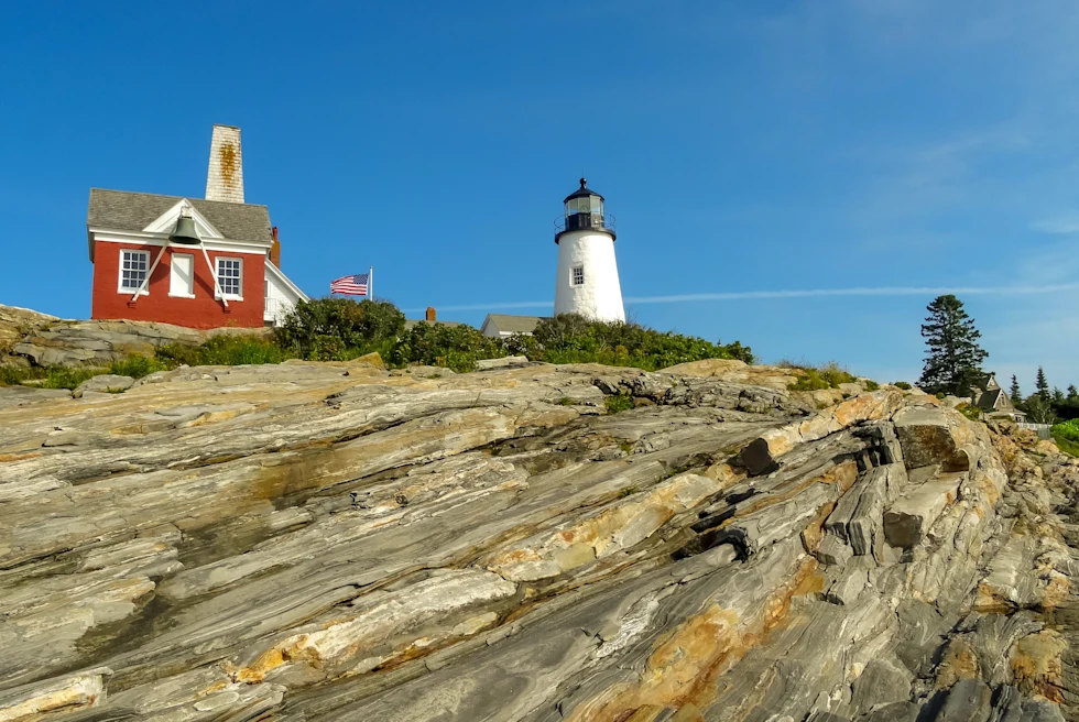 Red house with white lighthouse on rocky hill during daytime