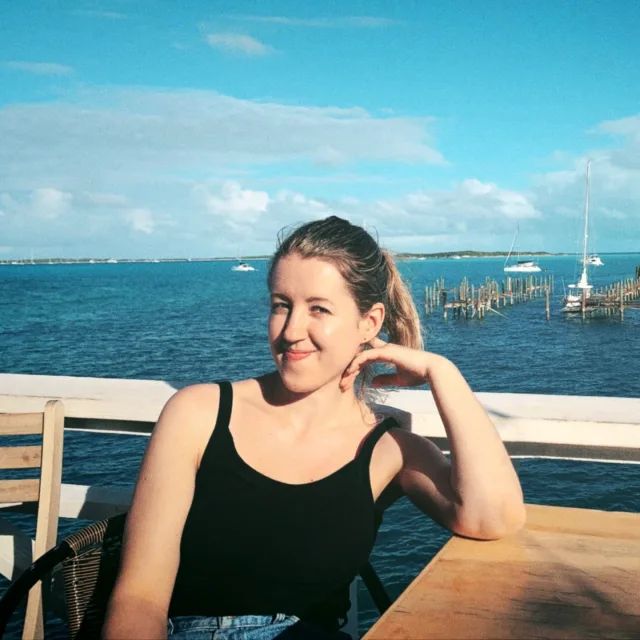 Iryna Apperson wears blank tank top sitting at a high top table on the ocean 