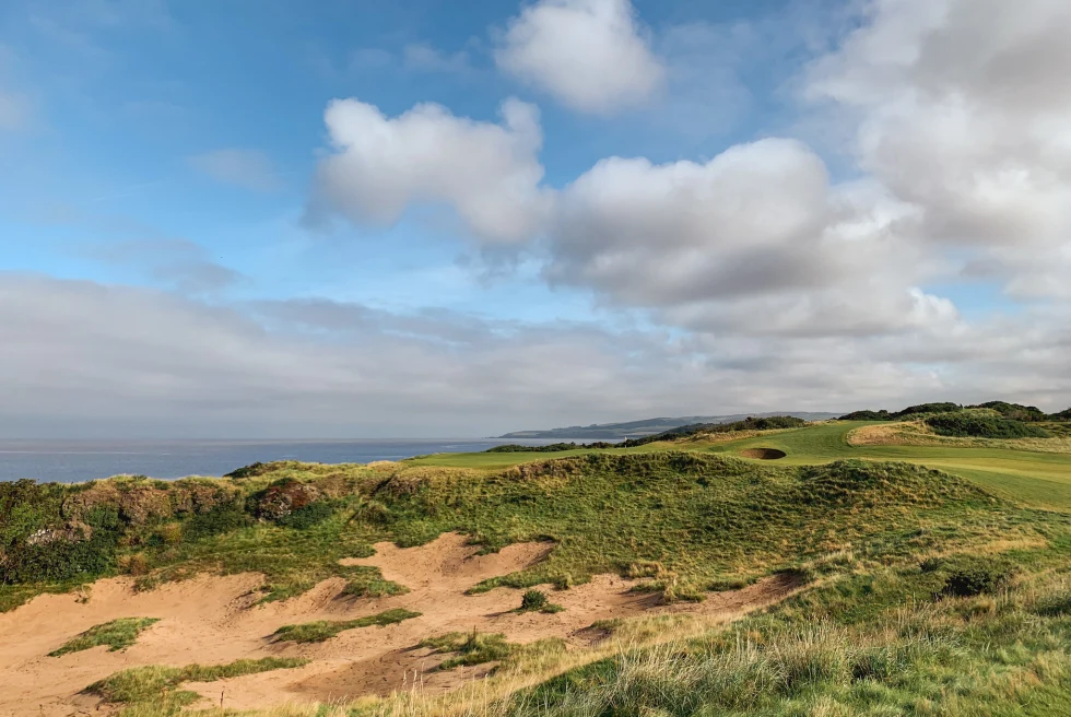 green grass golf course with tan sand and blue water in the distance