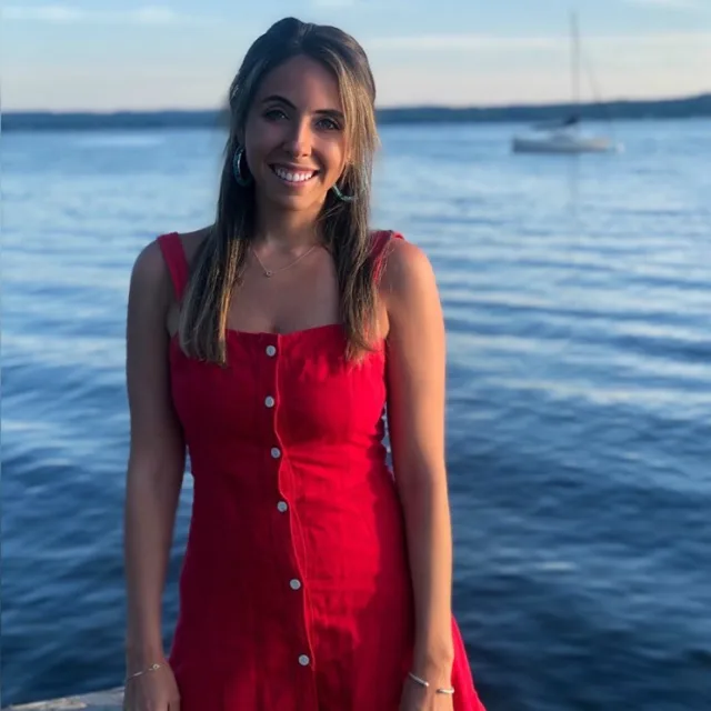 Travel advisor Cara Goodman wearing a red dress in front of a body of water