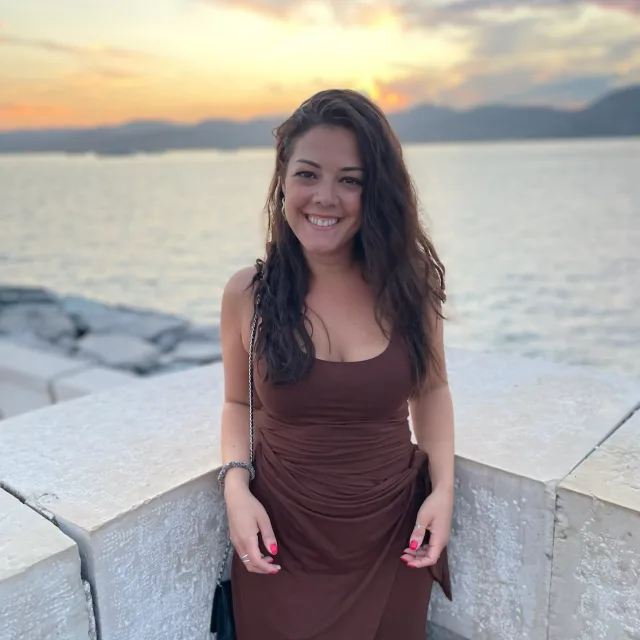 Travel Advisor Alison Pantano in a brown dress in front of the water at sunset.