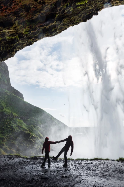 Two people stand behind cascading Seljalandfoss Waterfall in Iceland