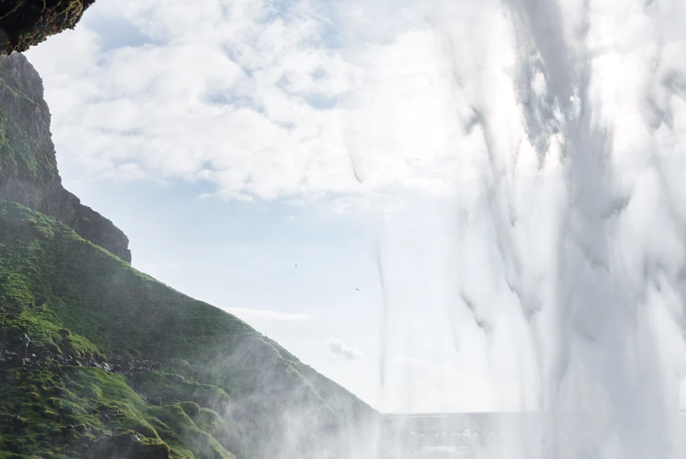 Two people stand behind cascading Seljalandfoss Waterfall in Iceland
