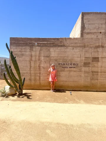 A girl standing in front of a hotel wall next to a large cactus. 