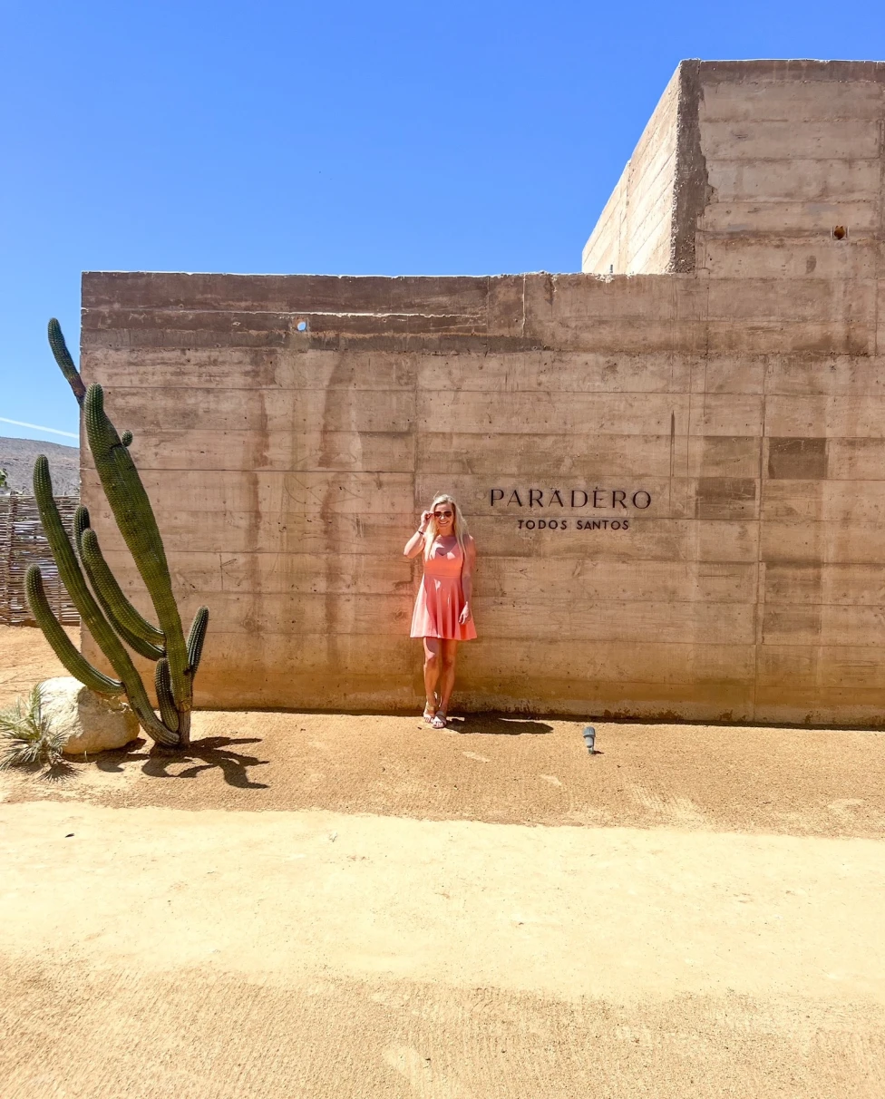 A girl standing in front of a hotel wall next to a large cactus. 