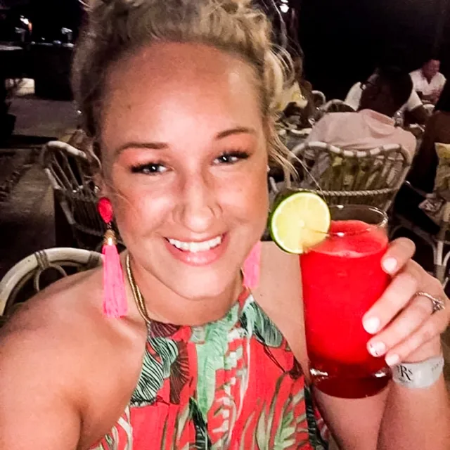 Travel Advisor Daesha Donze sitting at a restaurant in pink earrings holding a glass of red juice. 