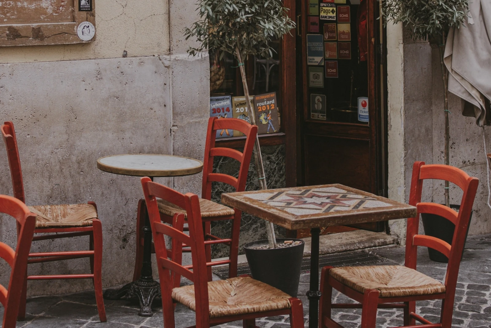 small tables and red chairs outside of a rustic Italian restaurant