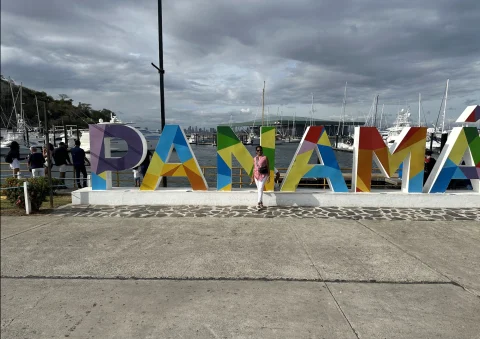 A view of a sign that says Panama in multi-colored paint. There is a cement sidewalk in front of it and a cloudy grey sky up above. 