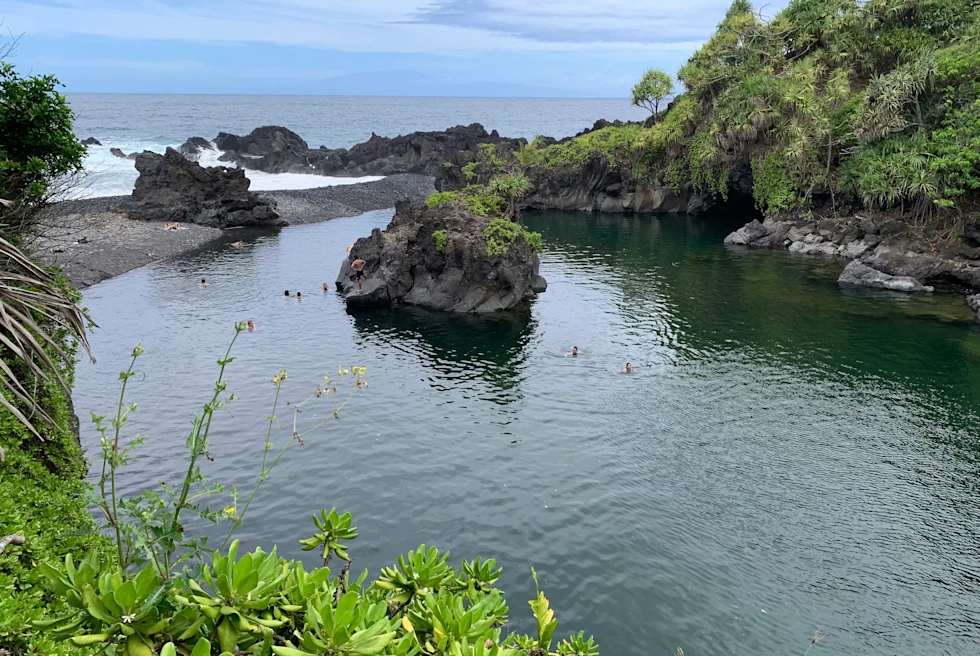 Pool of water next to body of water with people swimming during daytime