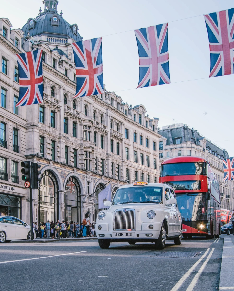 British flags hanging with cars on street next to tall buildings