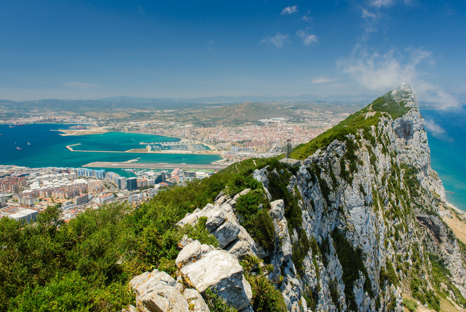 Large rock with green moss with city and body of water in background