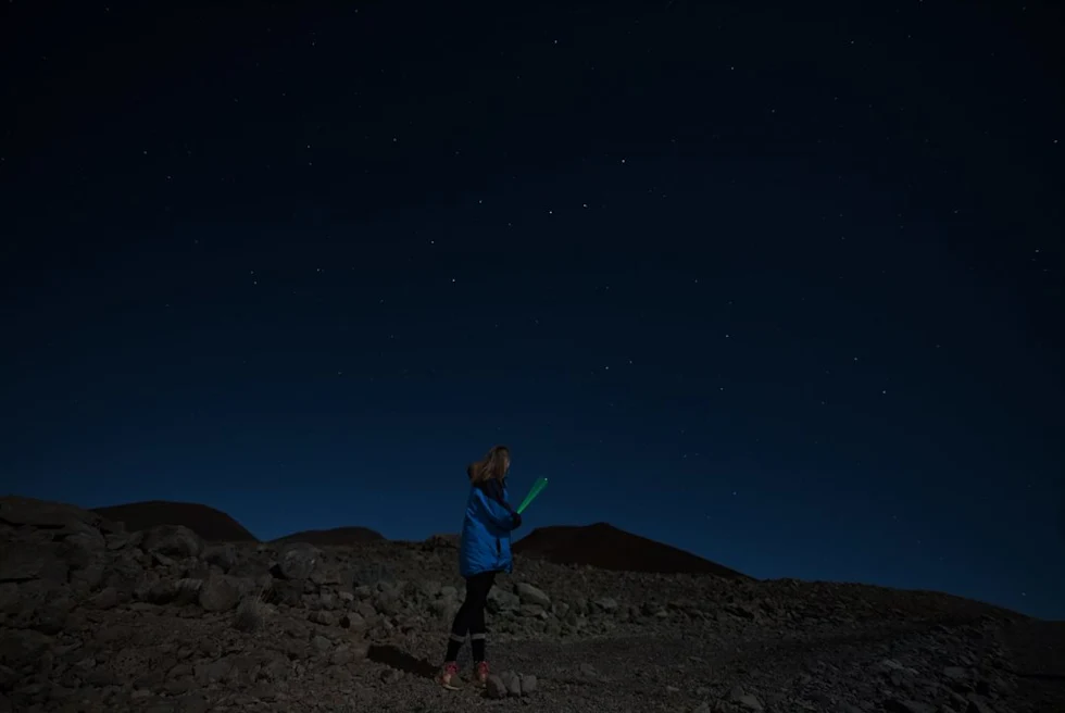Person standing on rocky ground with stars in the sky during nighttime