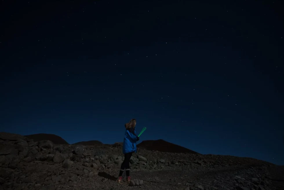 Person standing on rocky ground with stars in the sky during nighttime