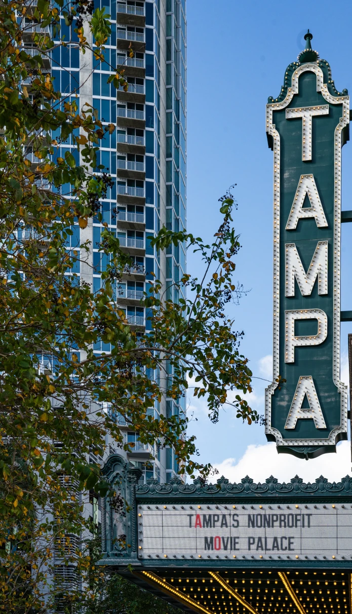 A sign board with the writing TAMPA on roadside and high rise building in the background.