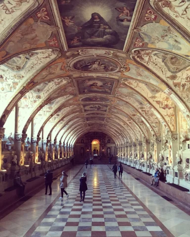 A photo of the inside of Residenz Museum in Munich. A large archway hall with beautiful art lining every angel of the arches. 