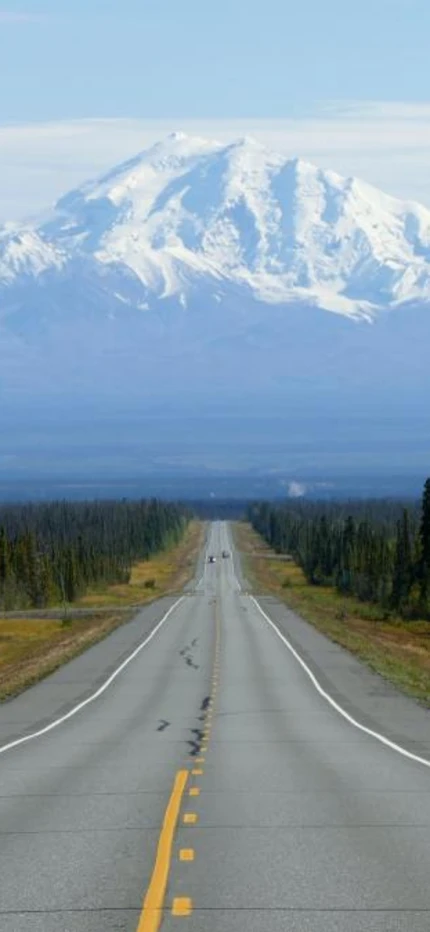 Wide road stretching to snowy mountains in Alaska. 