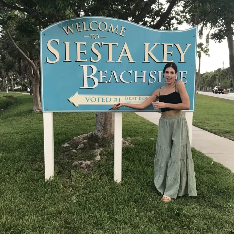 A woman stands before the “Welcome to Siesta Key Beach” sign, hinting at the beach’s allure and hospitality.