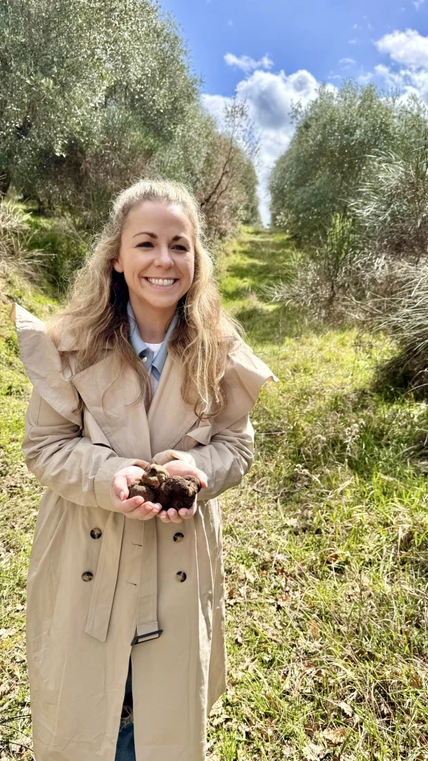 a woman in a tan coat holds black truffles in her hands