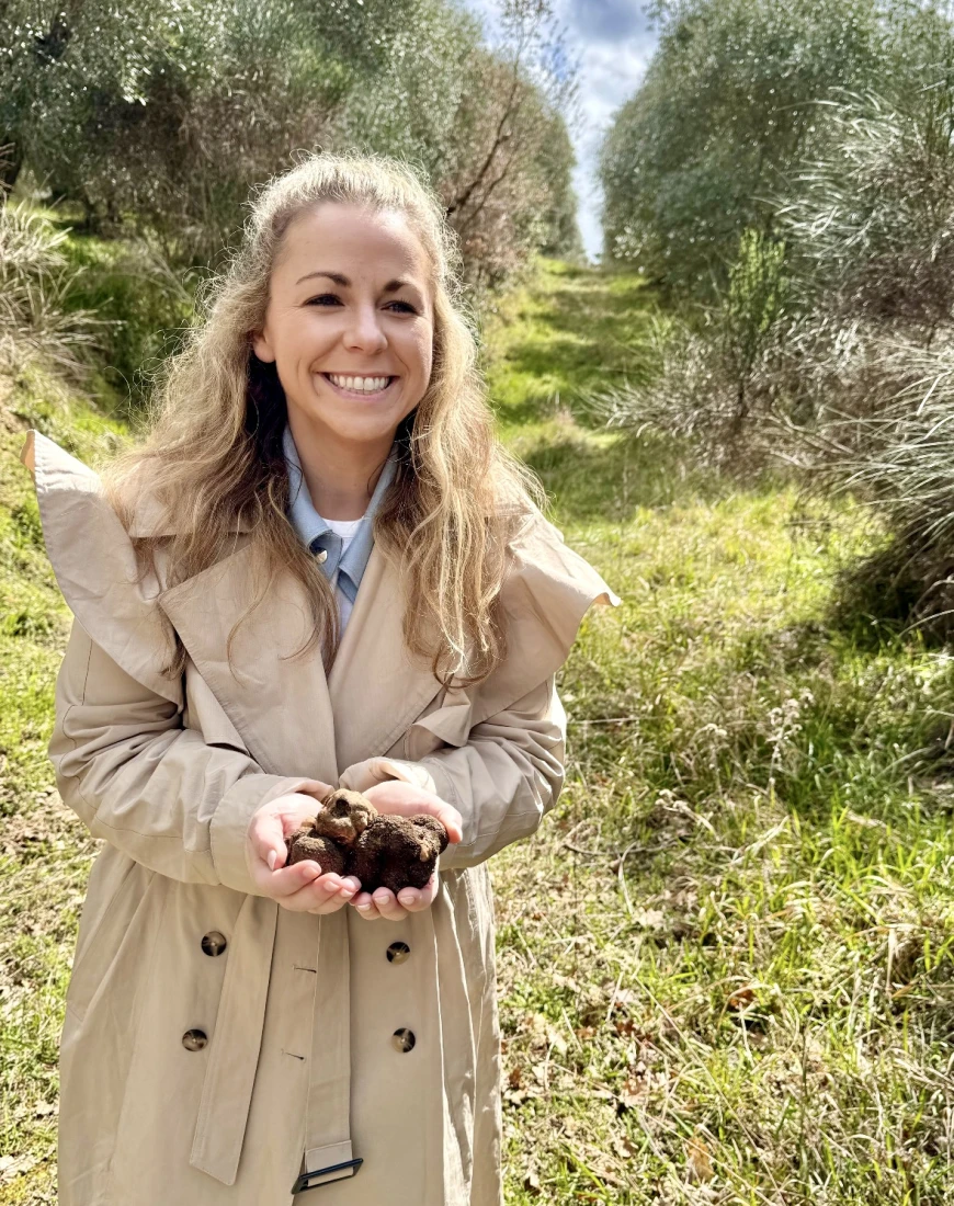 a woman in a tan coat holds black truffles in her hands