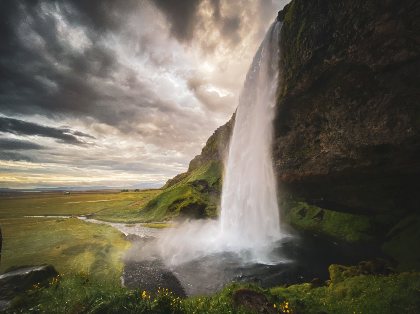 A white gushing waterfall with green grass and a cloudy sky in Iceland.