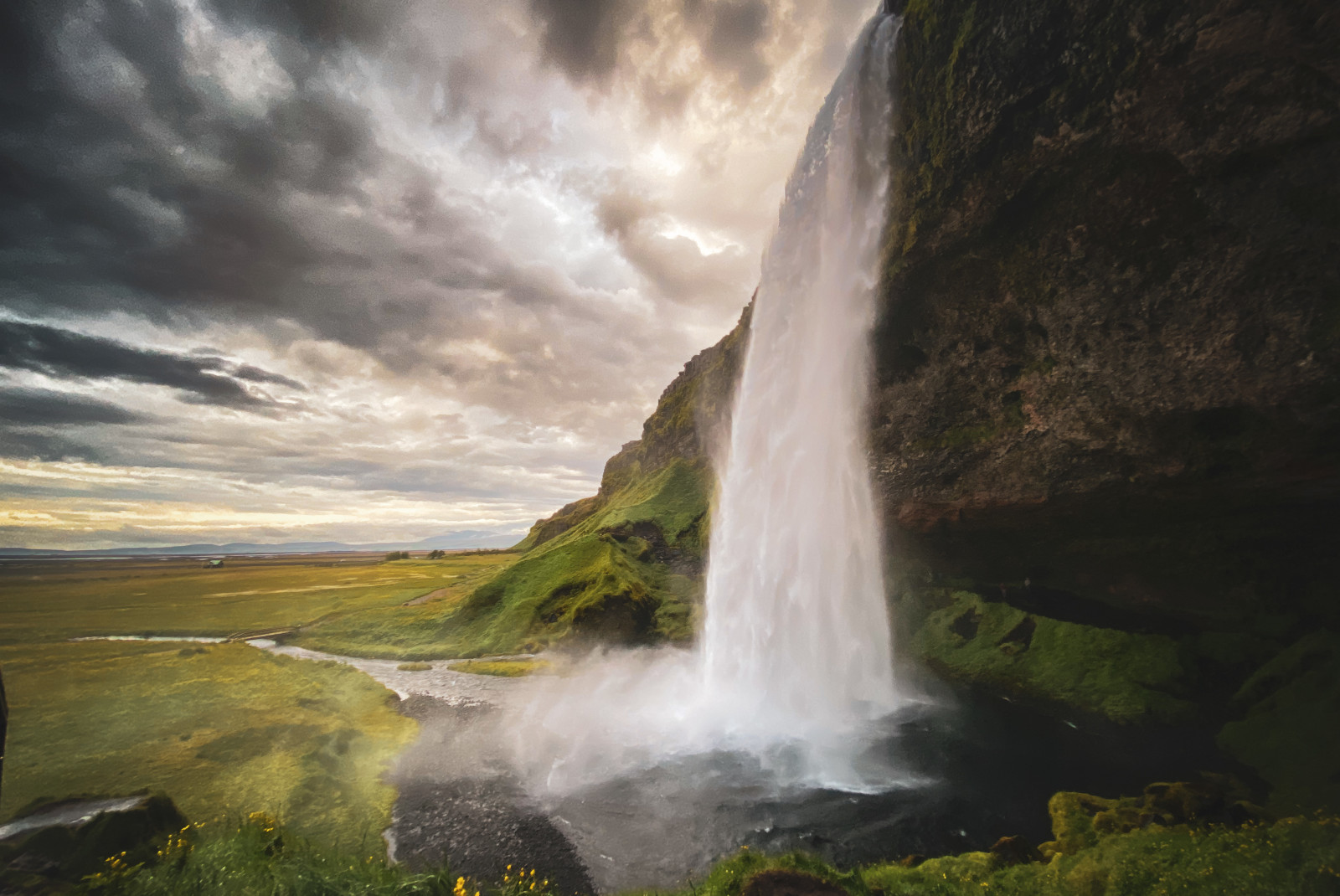 A white gushing waterfall with green grass and a cloudy sky in Iceland.
