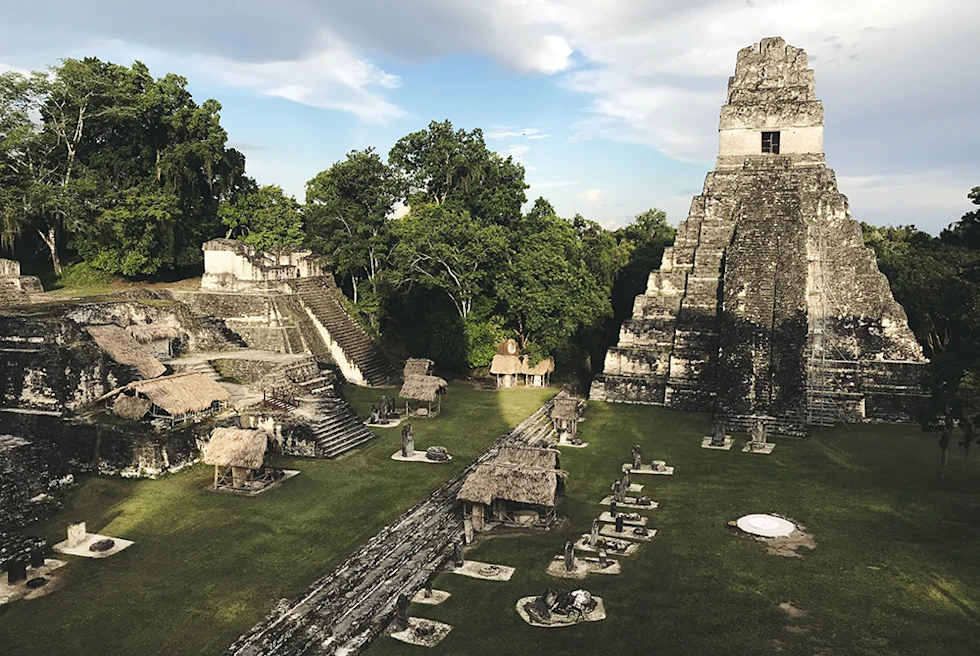 ancient grey and white ruins with green grass and tall trees in Guatemala