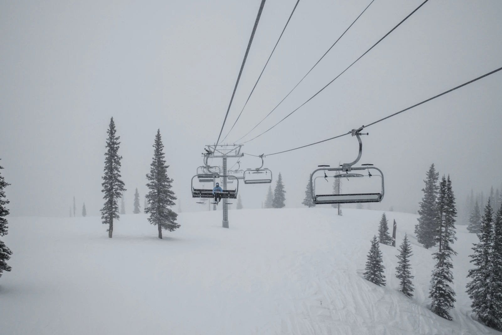 Snowy mountain with trees and a ski lift with cloudy skies