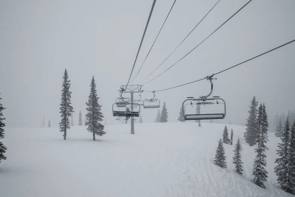 Snowy mountain with trees and a ski lift with cloudy skies