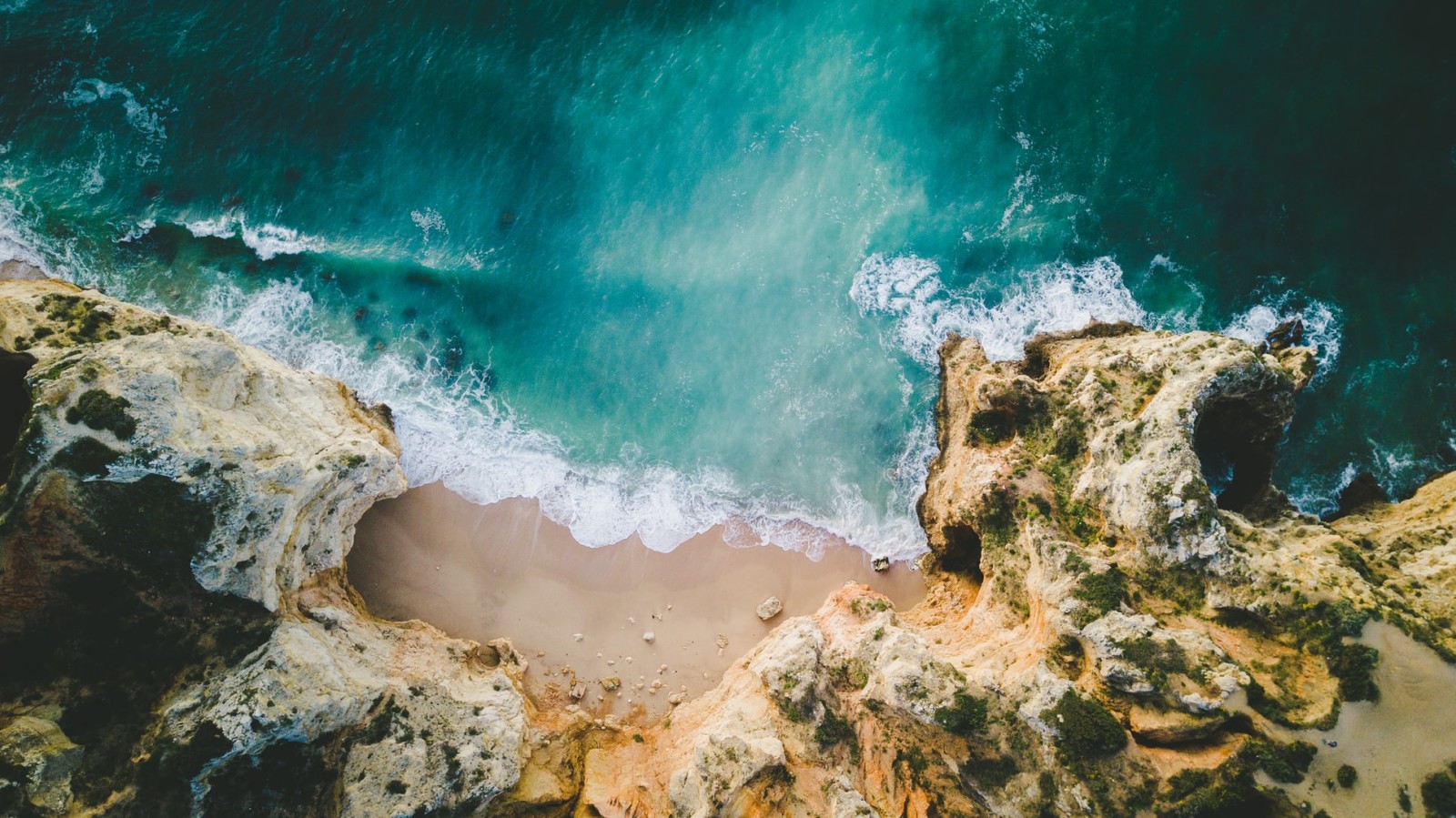 lagos Portugal aerial view of blue water with waves crashing into brown cliffs