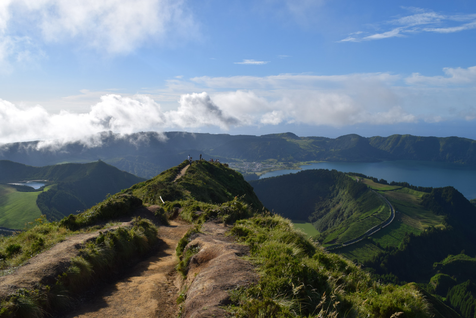 hilly mountains in Azores Portugal with green grass and brown dirt with an ocean below and blue sky with white clouds