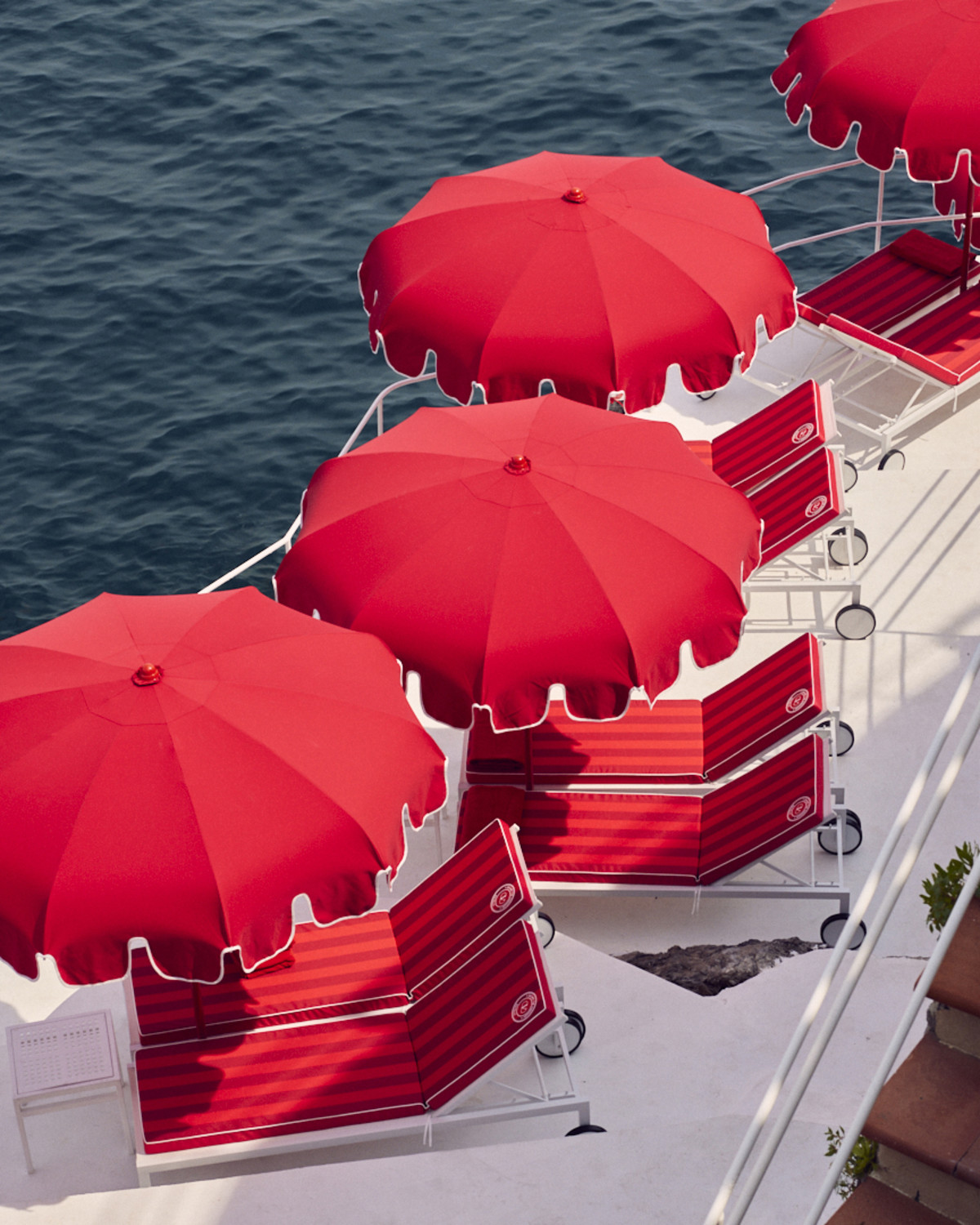 aerial view of red lounge chairs and red umbrellas overlooking the sea