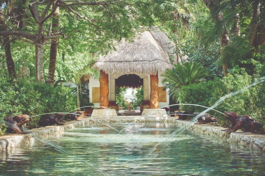 a turquoise reflection pool leading up to a thatched-roof structure in the jungle