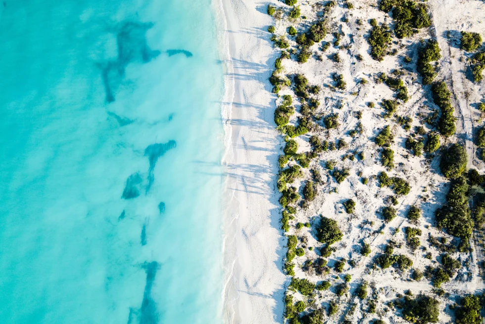 Aerial view of a beach with light blue clear water and white sand.