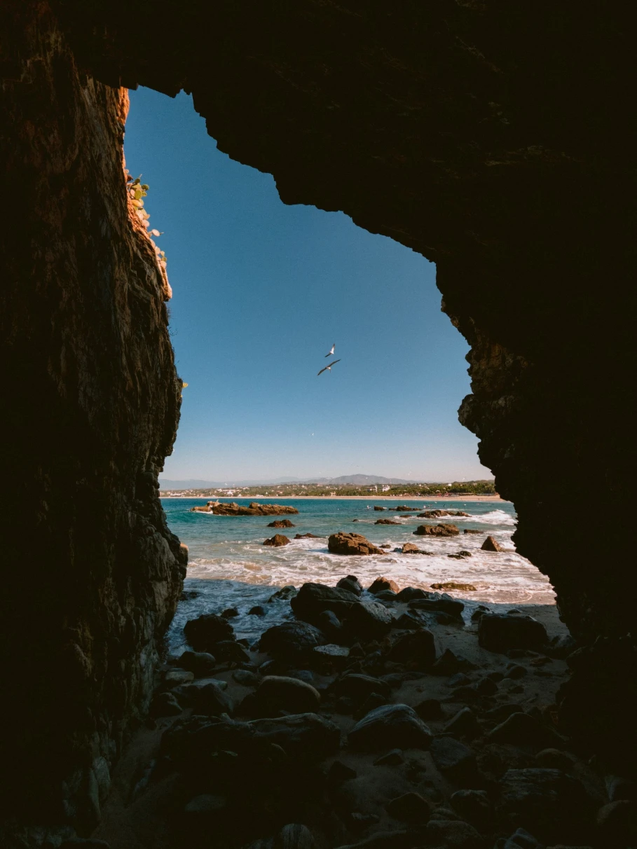 view through a rock formation of a rocky beach on a blue day with a hang glider 