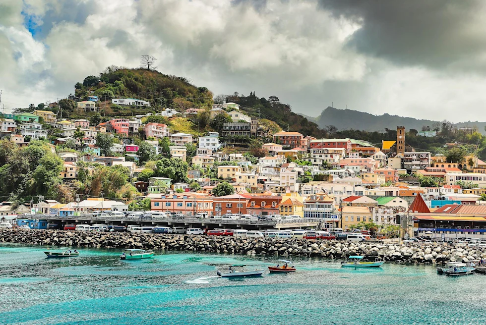 Colorful buildings with the ocean in the foreground and green hills in background in Grenada