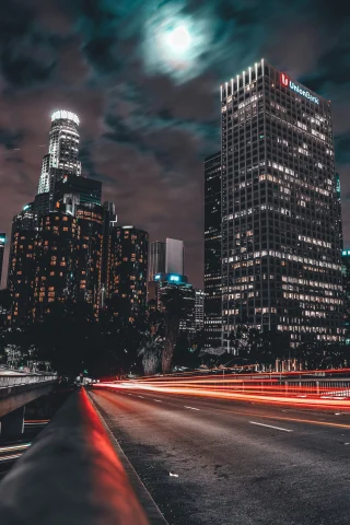 A picture of a time-lapse photo of cars passing on the road in front of skyscrapers during nighttime.