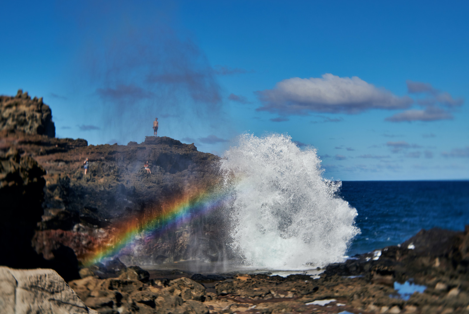 crashing waves next to rocky coastline with rainbow during daytime
