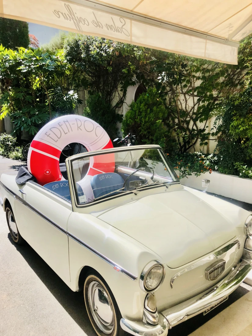 EdenRocRetroCar - a white classic convertible parked in the hotel driveway with a red-and-white pool inflatable in the background that says "Eden-Roc"
