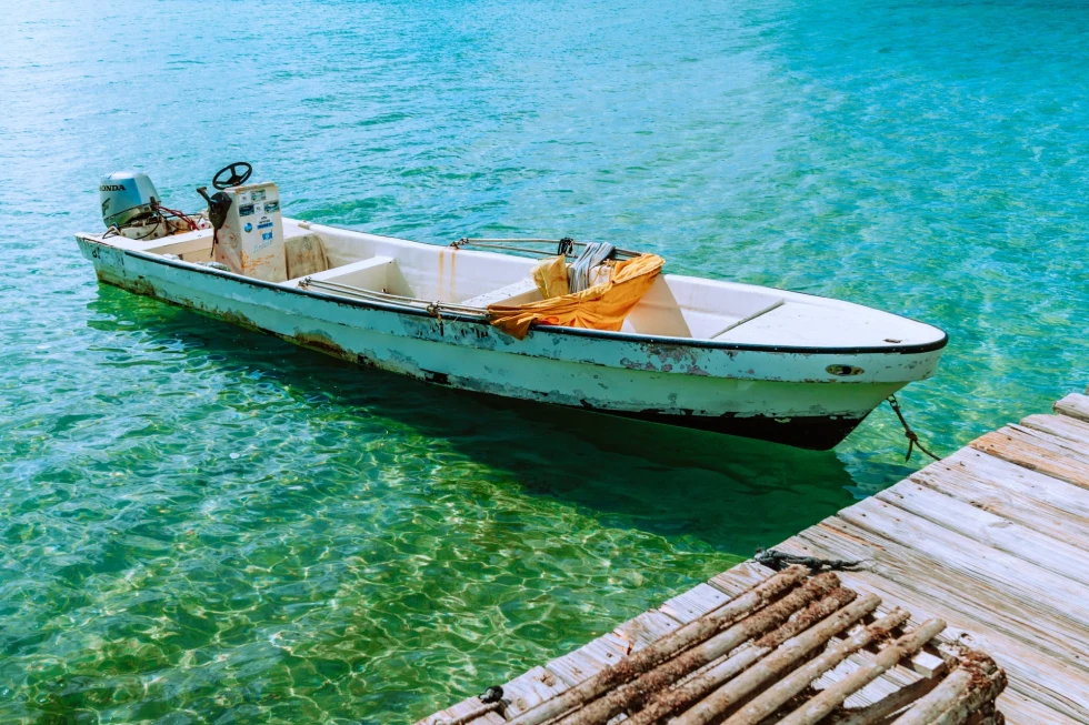 wooden row boat in turquoise ocean near a dock 