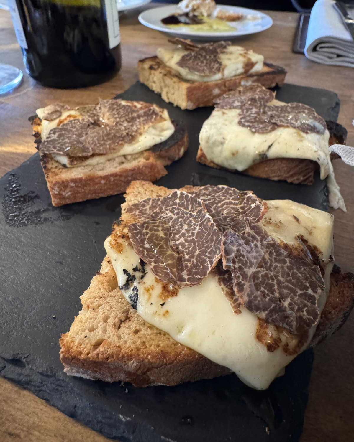 a black plate of toast covered in cheese and shave black truffles