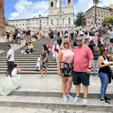 A picture of a couple with many people in the background, standing in front of an ancient Roman building.