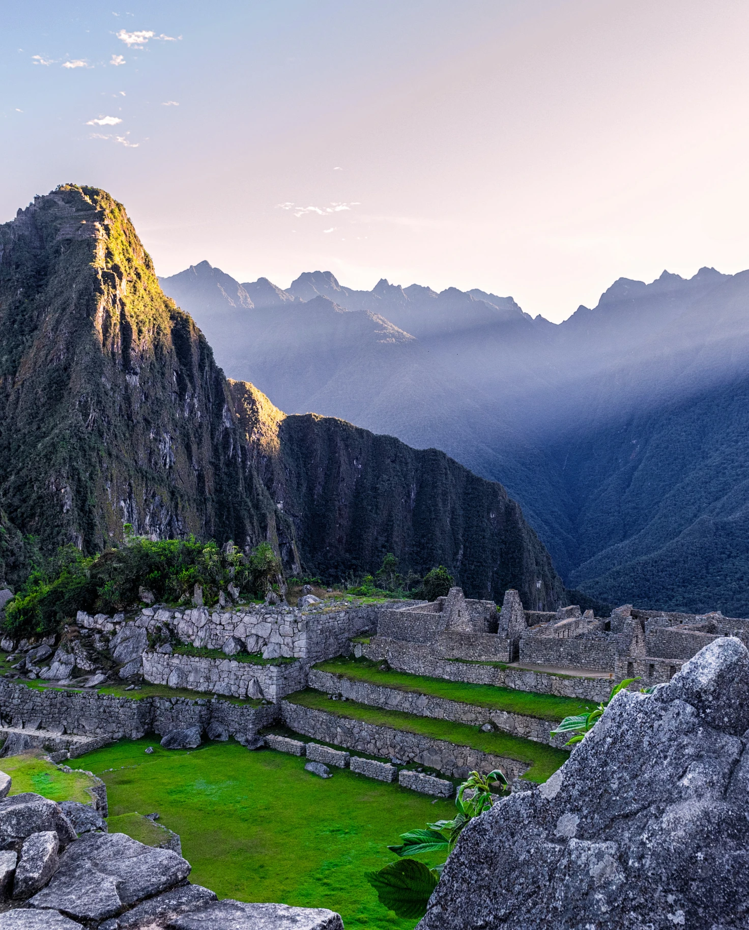 Machu Picchu in Peru green grass with grey stones and blue mountains with a beaming light
