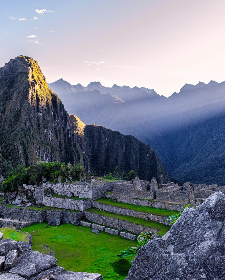 Machu Picchu in Peru green grass with grey stones and blue mountains with a beaming light