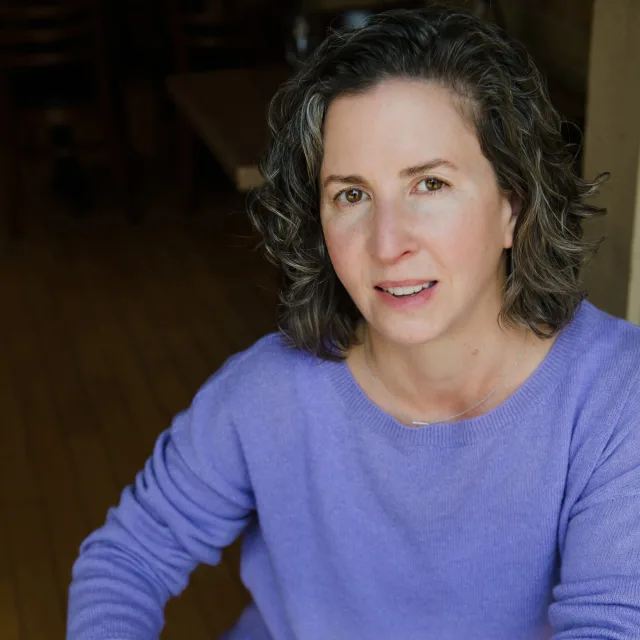 A woman in a purple shirt holds an orange mug of coffee