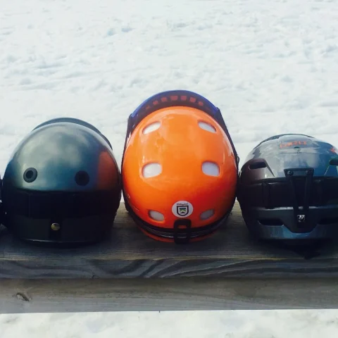 A picture of seven different colored ski helmets lined up on a wooden bench.