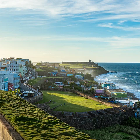 Puerto Rico overlook blue and white ocean and sky with white buildings and green grass overlooking on cliff