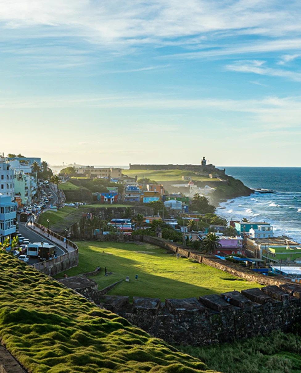 Puerto Rico overlook blue and white ocean and sky with white buildings and green grass overlooking on cliff